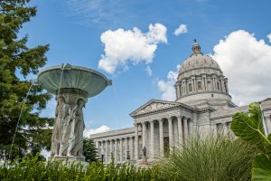 The Missouri State Capital Building in Jefferson City Columbia. A fountain stands in front with 4 engraved figures on it.