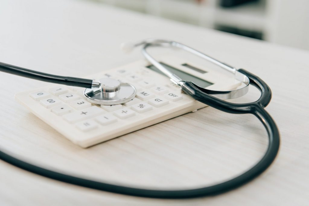 close up of stethoscope lying on calculator, health insurance concept | Winter-Dent close up of stethoscope lying on calculator, health insurance concept